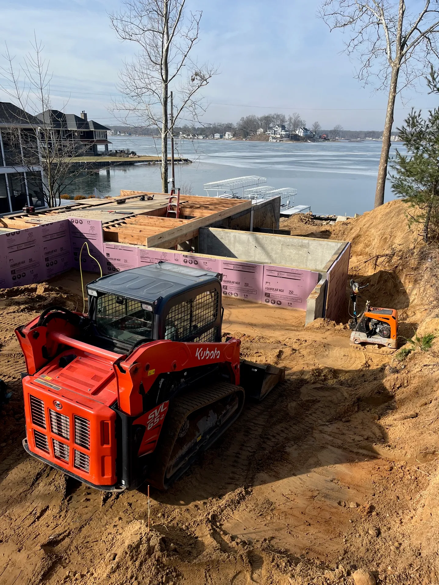 Excavator and skid steer preparing a basement foundation with a dump trailer on site at a Kalamazoo home