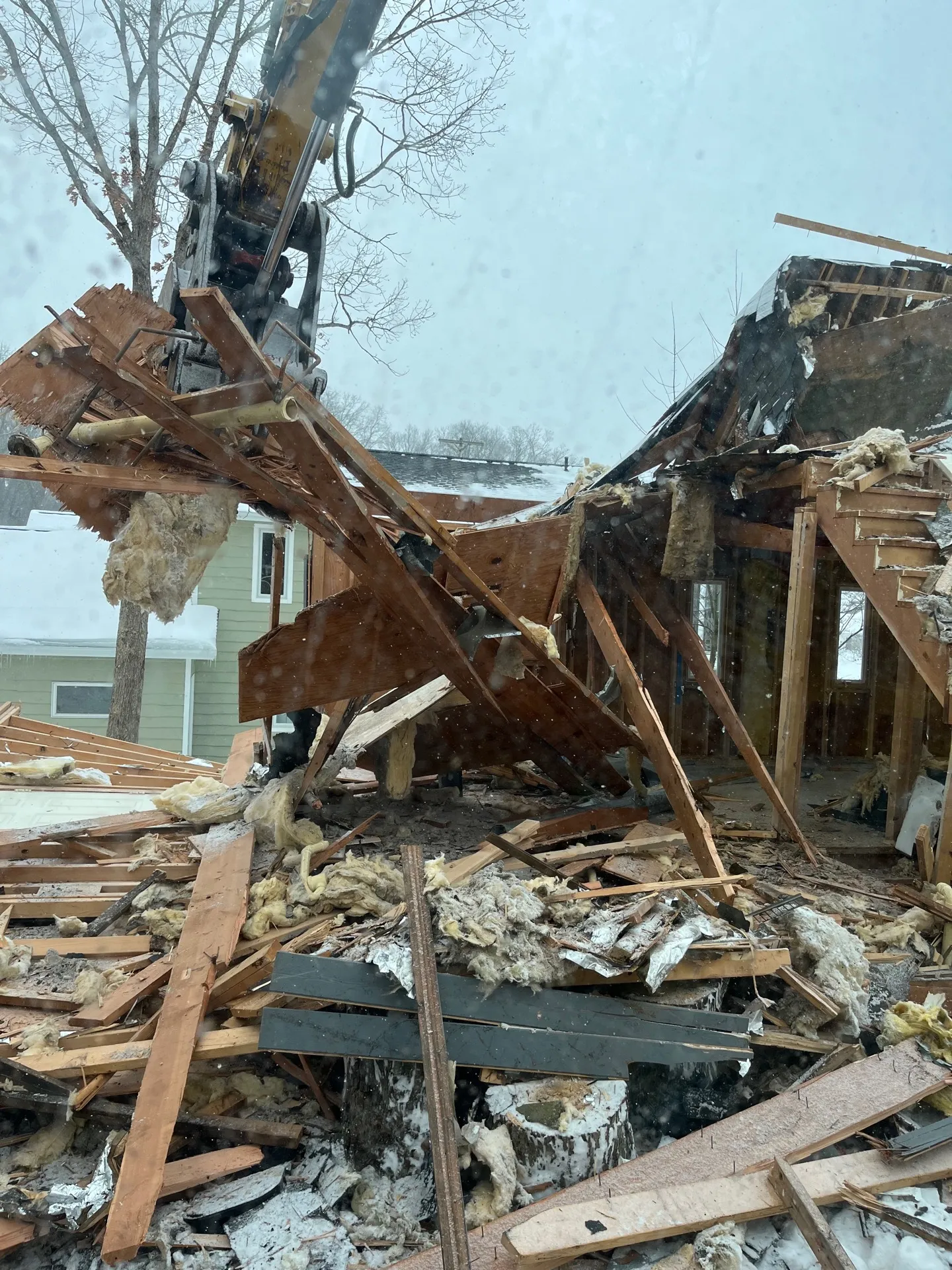 Excavator and skid steer clearing storm debris from a damaged Kalamazoo property with a dump trailer on site